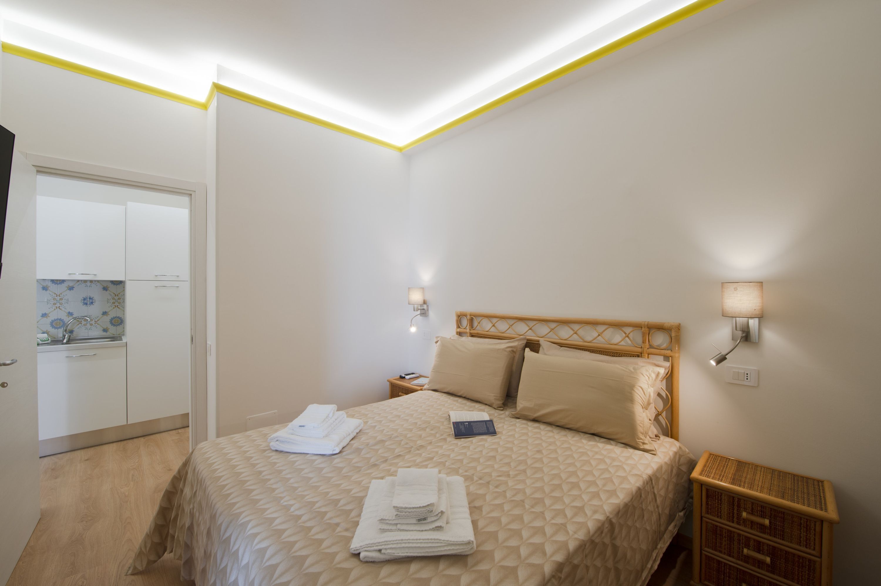 Een slaapkamer met een bed, bedlampen, een nachtkastje en een klein houten bijzettafeltje.