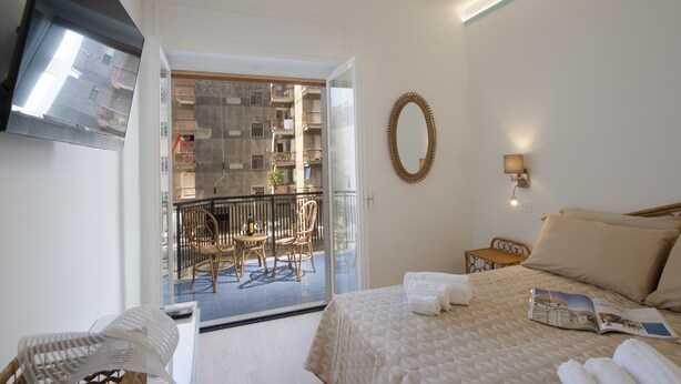 Une chambre d’hôtel avec un lit, une chaise, une table et un balcon donnant sur la ville.