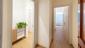 Un couloir avec un plancher en bois, des murs blancs et une plante posée sur une commode.