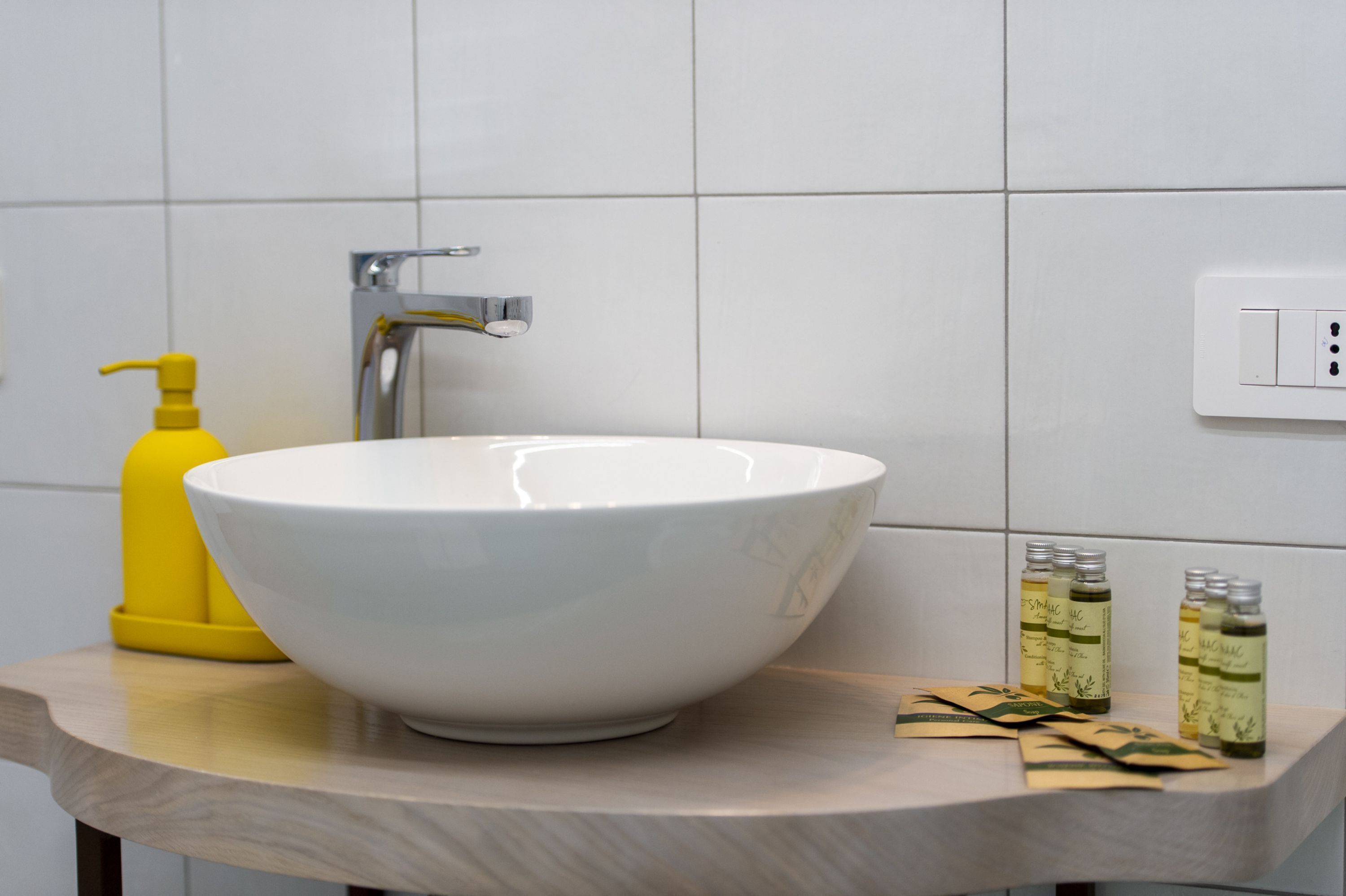 A bathroom with a white sink, a yellow soap dispenser, and several bottles of liquid soap on the countertop.