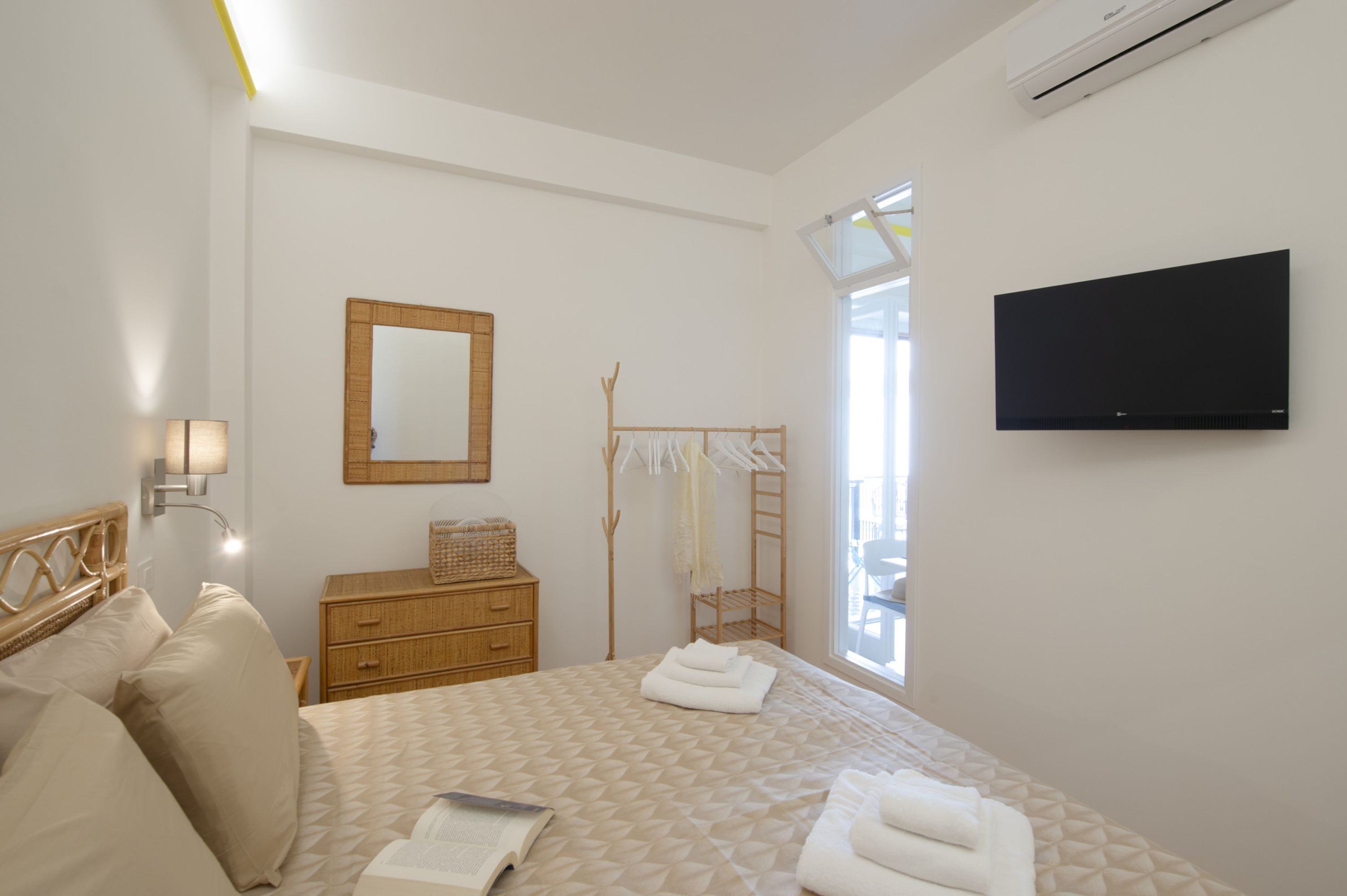 Une chambre à coucher avec un lit, une commode en bois, un miroir, une télévision et une fenêtre.