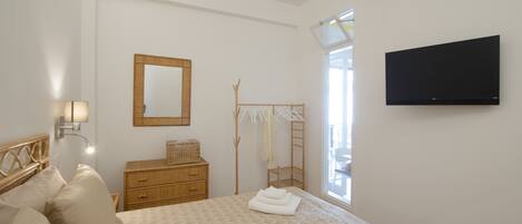 Une chambre à coucher avec un lit, une commode en bois, un miroir, une télévision et une fenêtre.