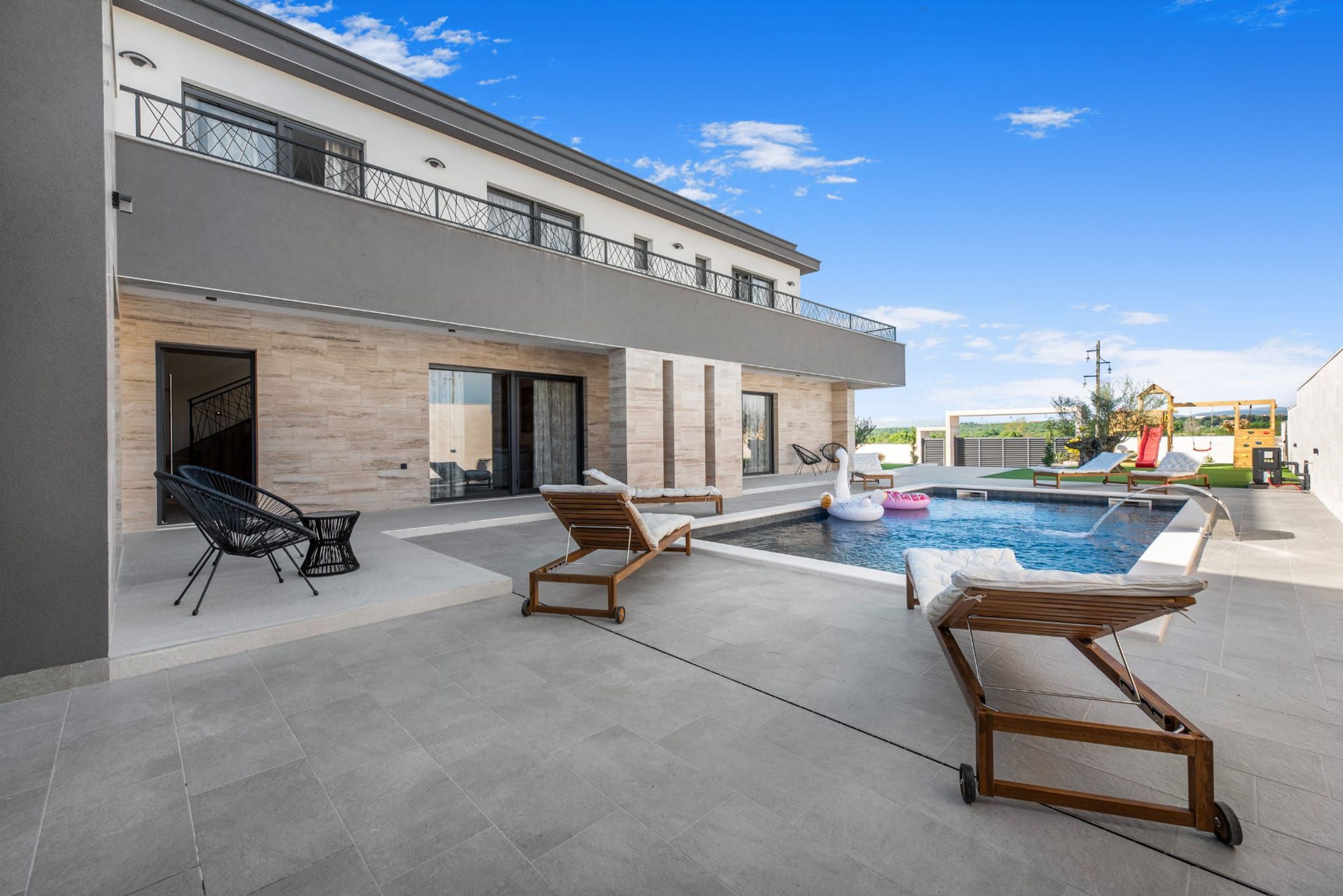 Una casa moderna con piscina, mobiliario exterior y un balcón.