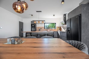 Eine moderne Küche mit einem Holztisch, grau gepolsterten Stühlen und einem schwarzen Kühlschrank.