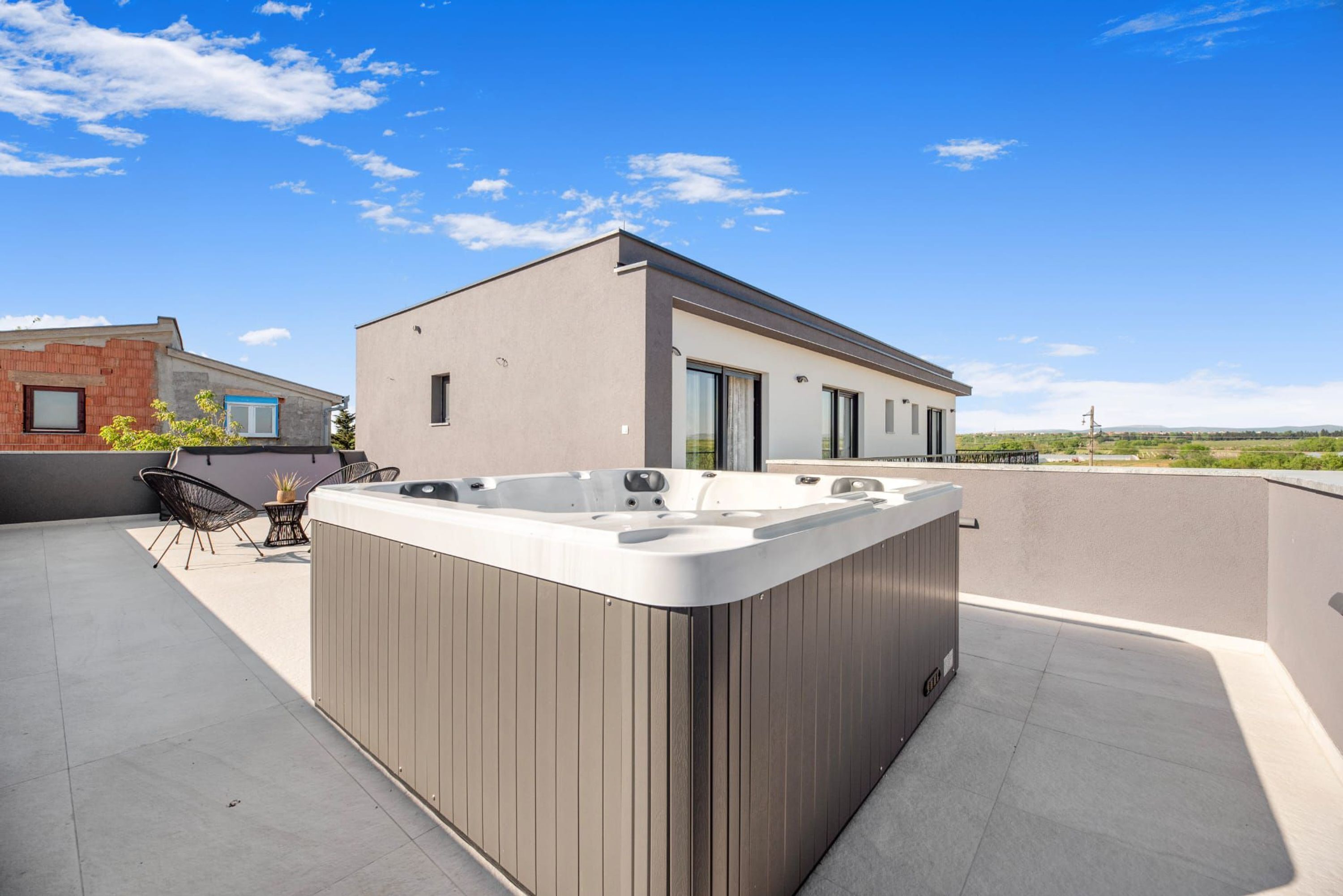 A modern building with a rooftop patio featuring a hot tub, outdoor seating, and a clear view of the surrounding landscape.