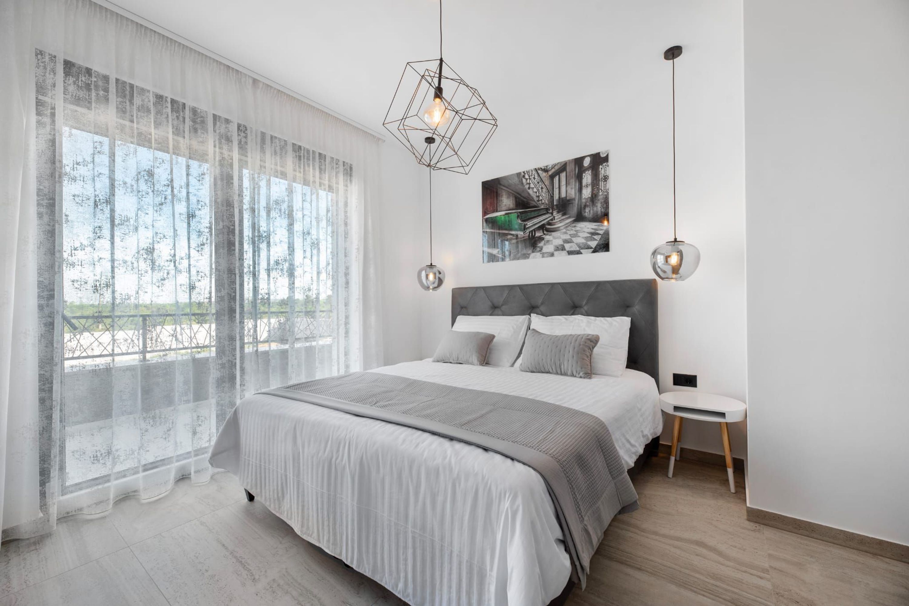 A modern bedroom with a large bed, a view of the outdoors, and a painting on the wall.