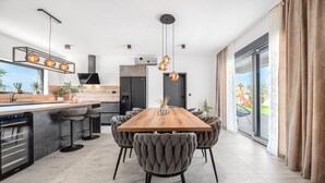 Une cuisine moderne avec une table à manger en bois, des chaises à revêtement gris et des luminaires suspendus.