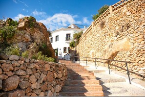 Una escalera de piedra que conduce a un edificio blanco con balcón, rodeado de terreno rocoso y vegetación.
