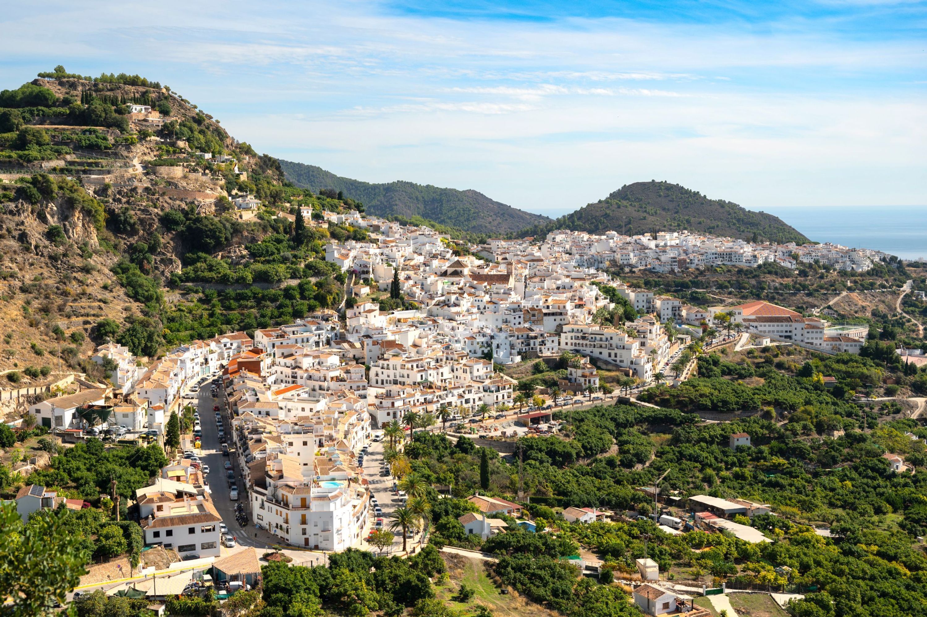 A coastal town with white buildings, narrow streets, and a hilly backdrop.