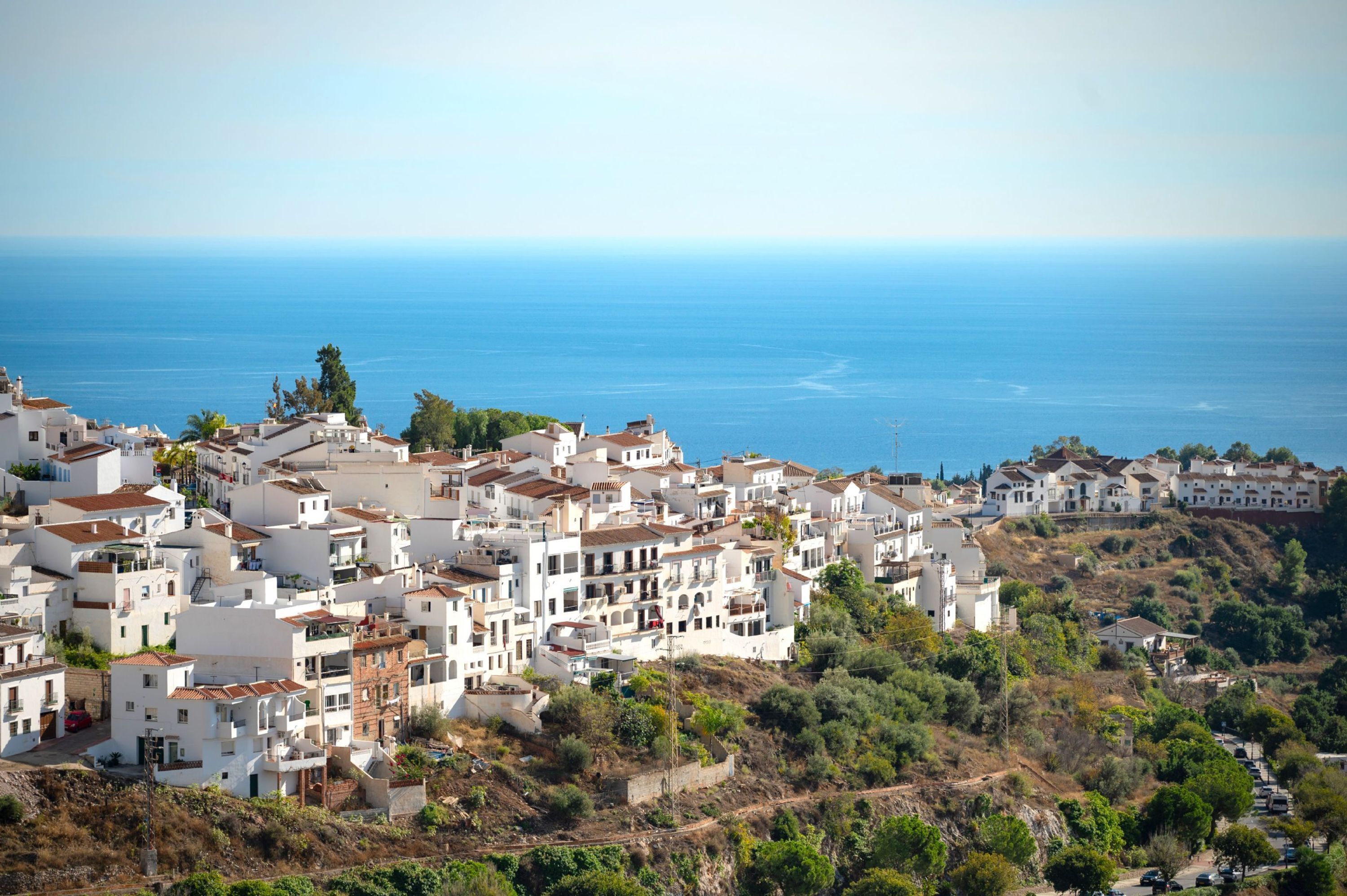 Un pueblo costero con edificios blancos, vista despejada al mar y un paisaje montañoso.