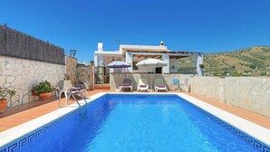 A swimming pool with lounge chairs and umbrellas, surrounded by stone walls and potted plants. - Casa La Era in Frigiliana (Frigiliana)