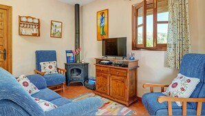 A cozy living room with blue upholstered furniture, a television, a fireplace, and a window with curtains. - Casa La Era in Frigiliana (Frigiliana)
