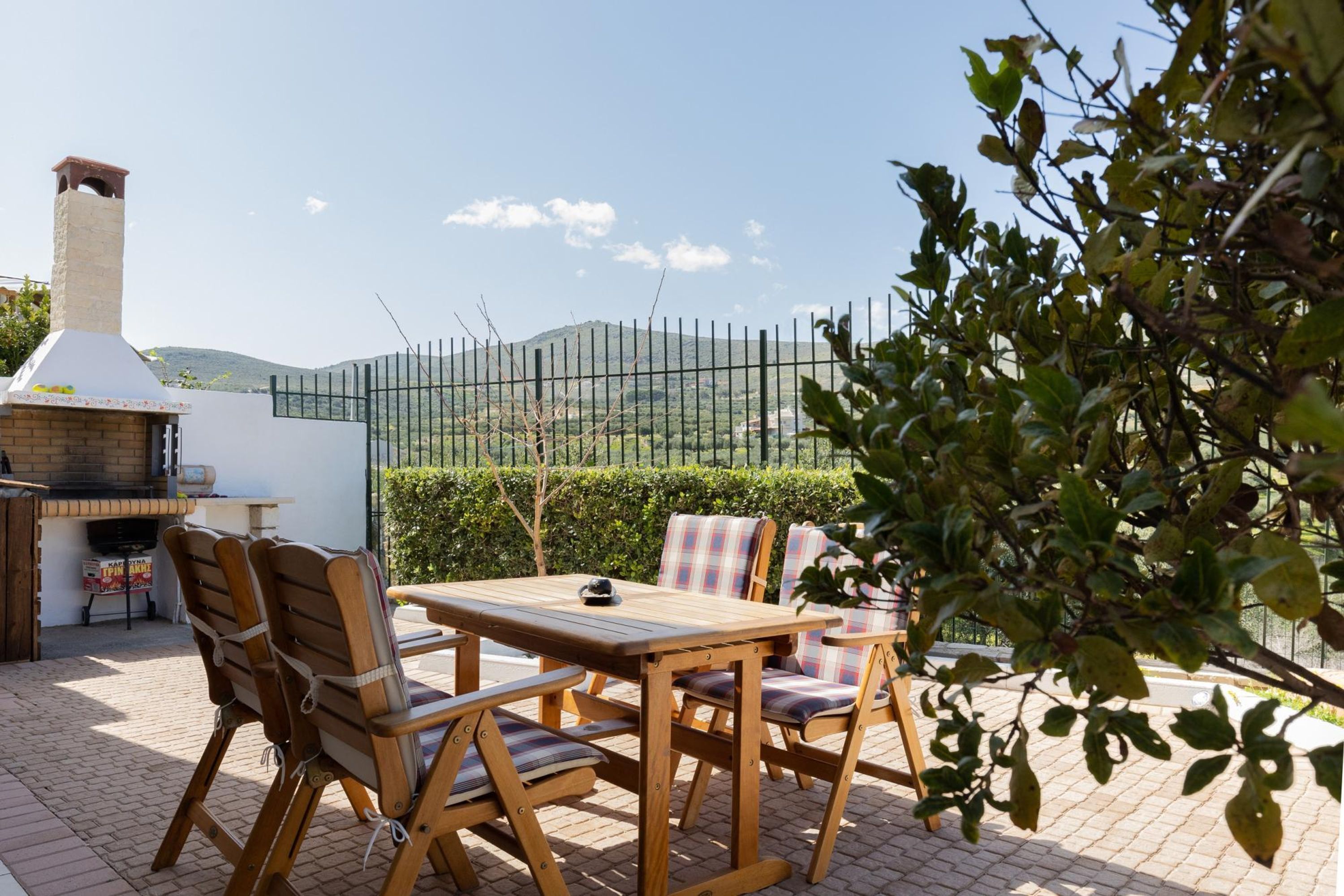 Un patio al aire libre con una mesa y sillas de madera, una parrilla de barbacoa y vistas a colinas al fondo.