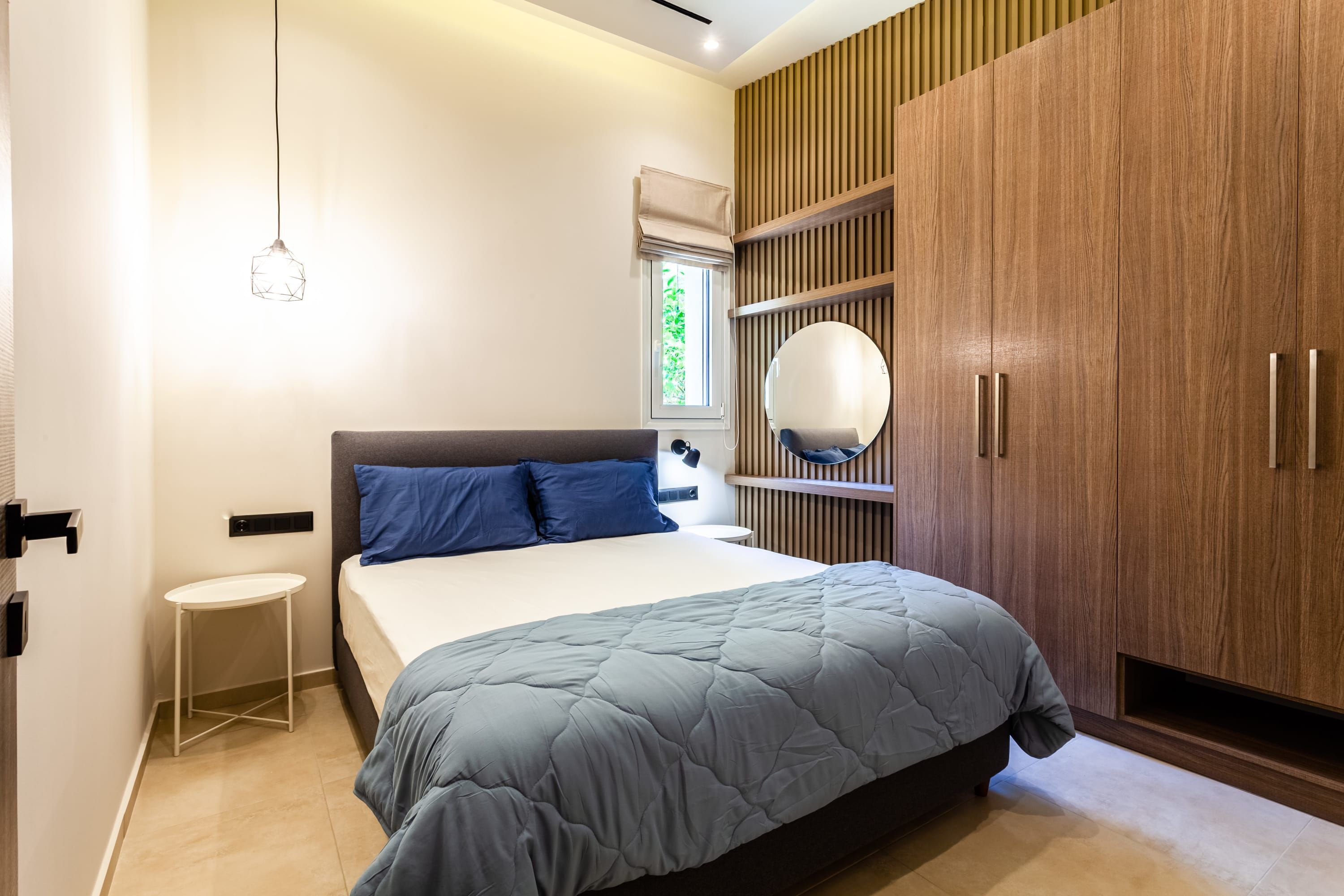Un dormitorio moderno con cama, mesita de noche, armario y lámpara colgante.