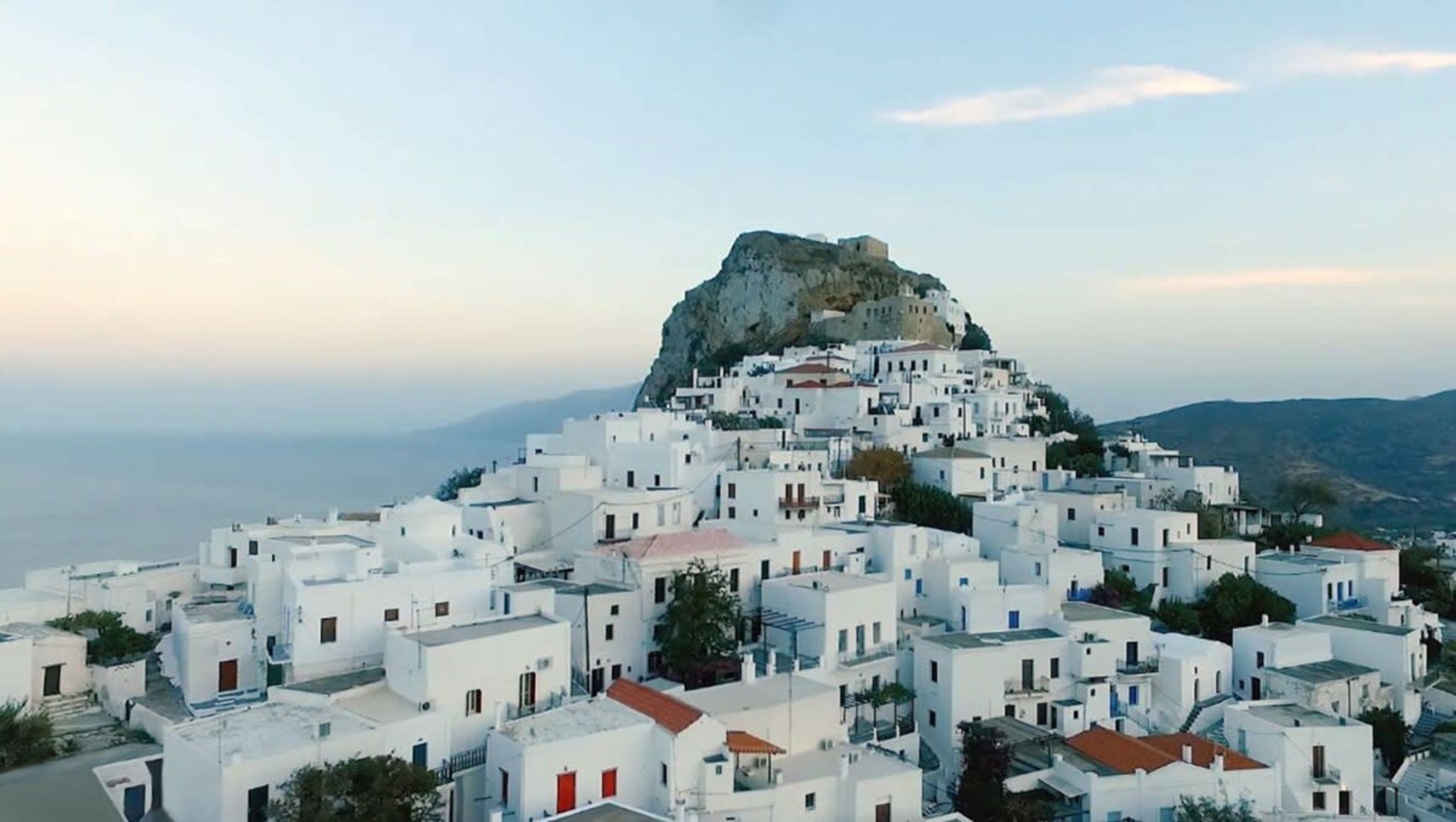 A coastal village with white buildings clustered around a rocky hill.