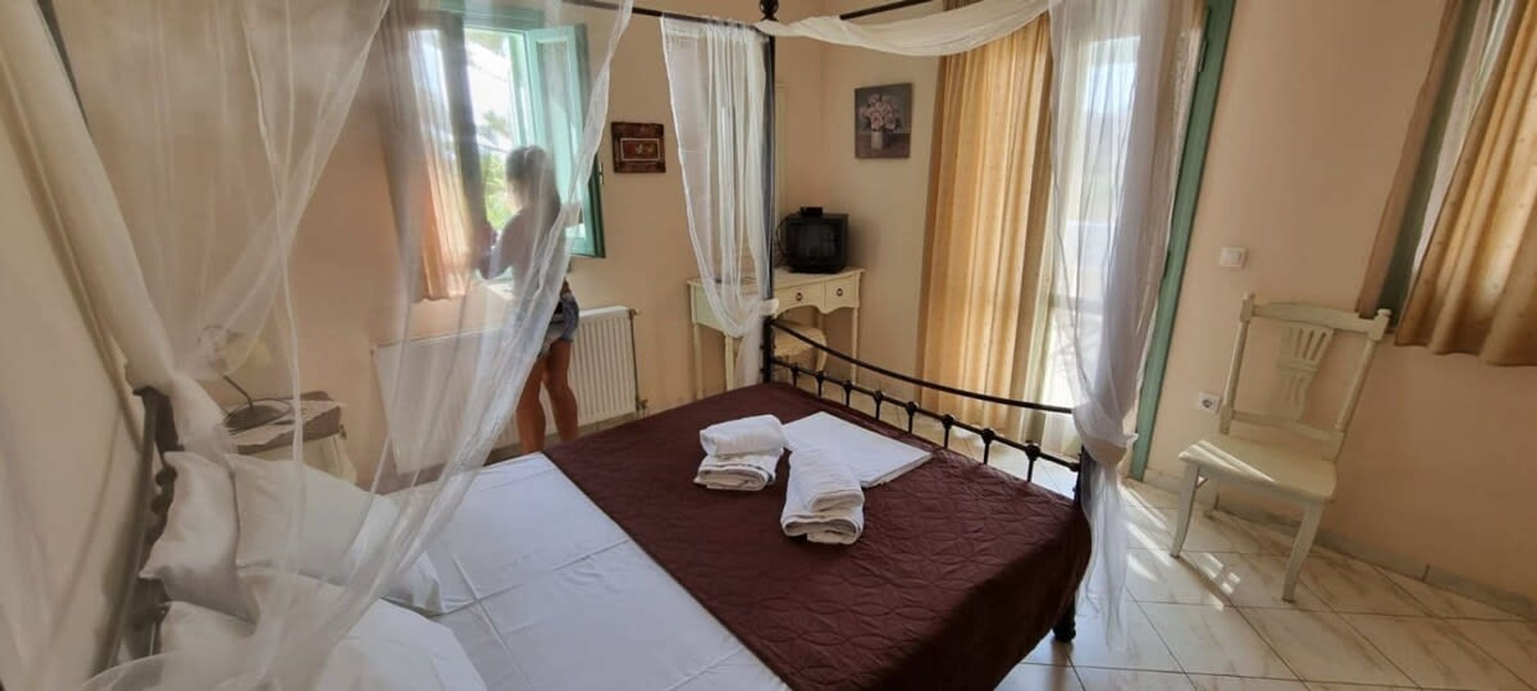 A bedroom with a bed, white curtains, a television, and a chair.