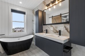 Ein modernes Badezimmer mit einer freistehenden Badewanne, einem Doppelwaschtisch mit großem Spiegel und einem Fenster mit Ausblick nach draußen.