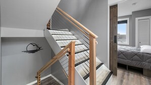 Ein modernes Schlafzimmer mit schrägen Wänden, einer Holztreppe und einem Bett mit grauer Bettdecke.