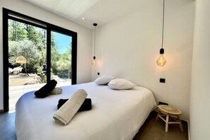 A modern bedroom with a large bed, a small stool, and a view of the outdoors through a large window. - Casa di Macchjerolu - 8 Pers (Sotta)