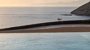 Escena costera con un muro de piedra, mar tranquilo y un velero.