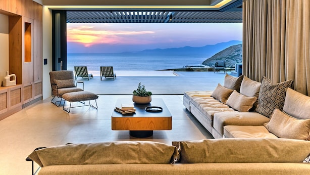 Una sala moderna con un ventanal grande con vistas al mar, un sofá, sillones y una mesa de centro.