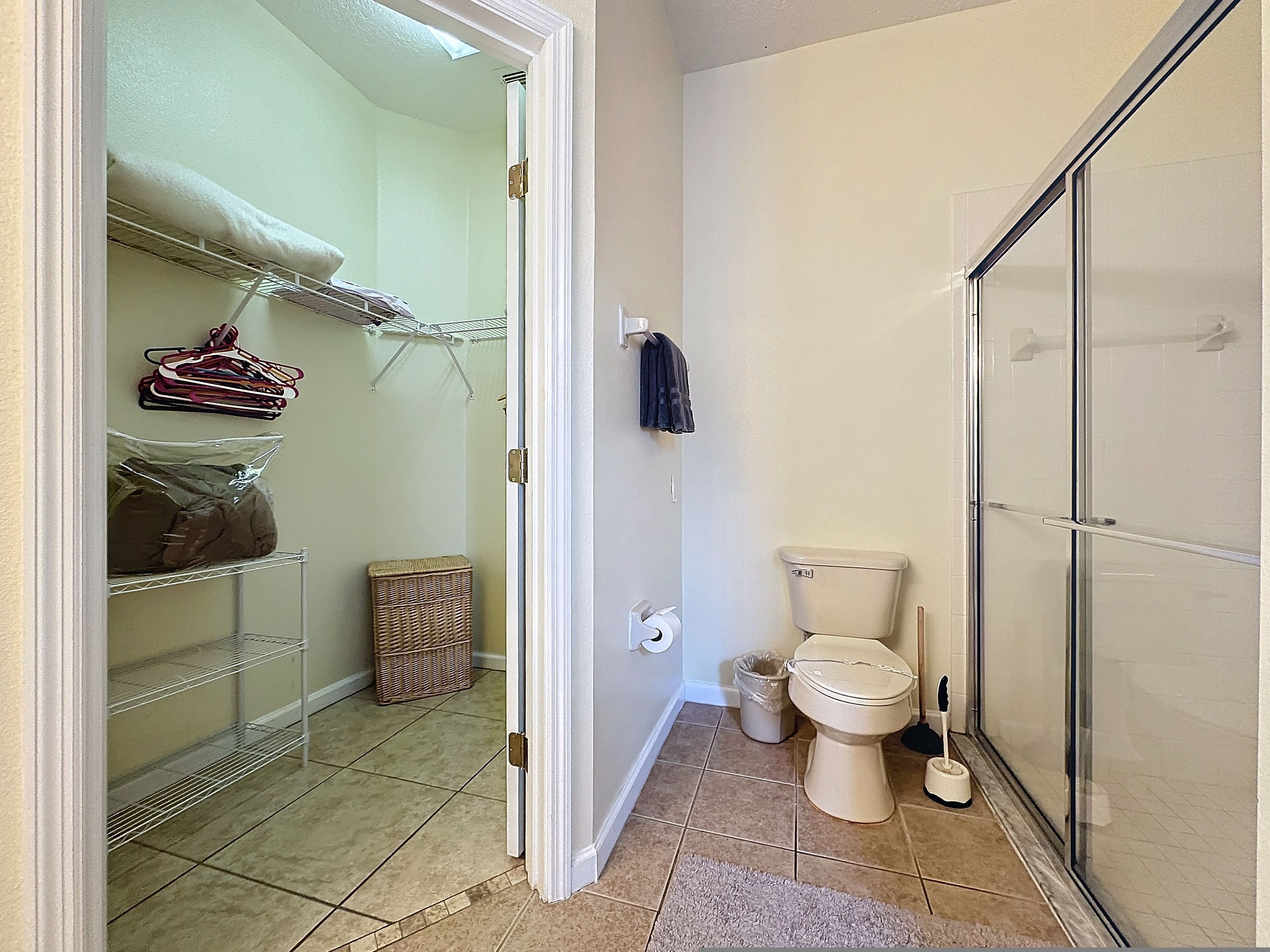 A bathroom with a toilet, shower, and storage shelves.
