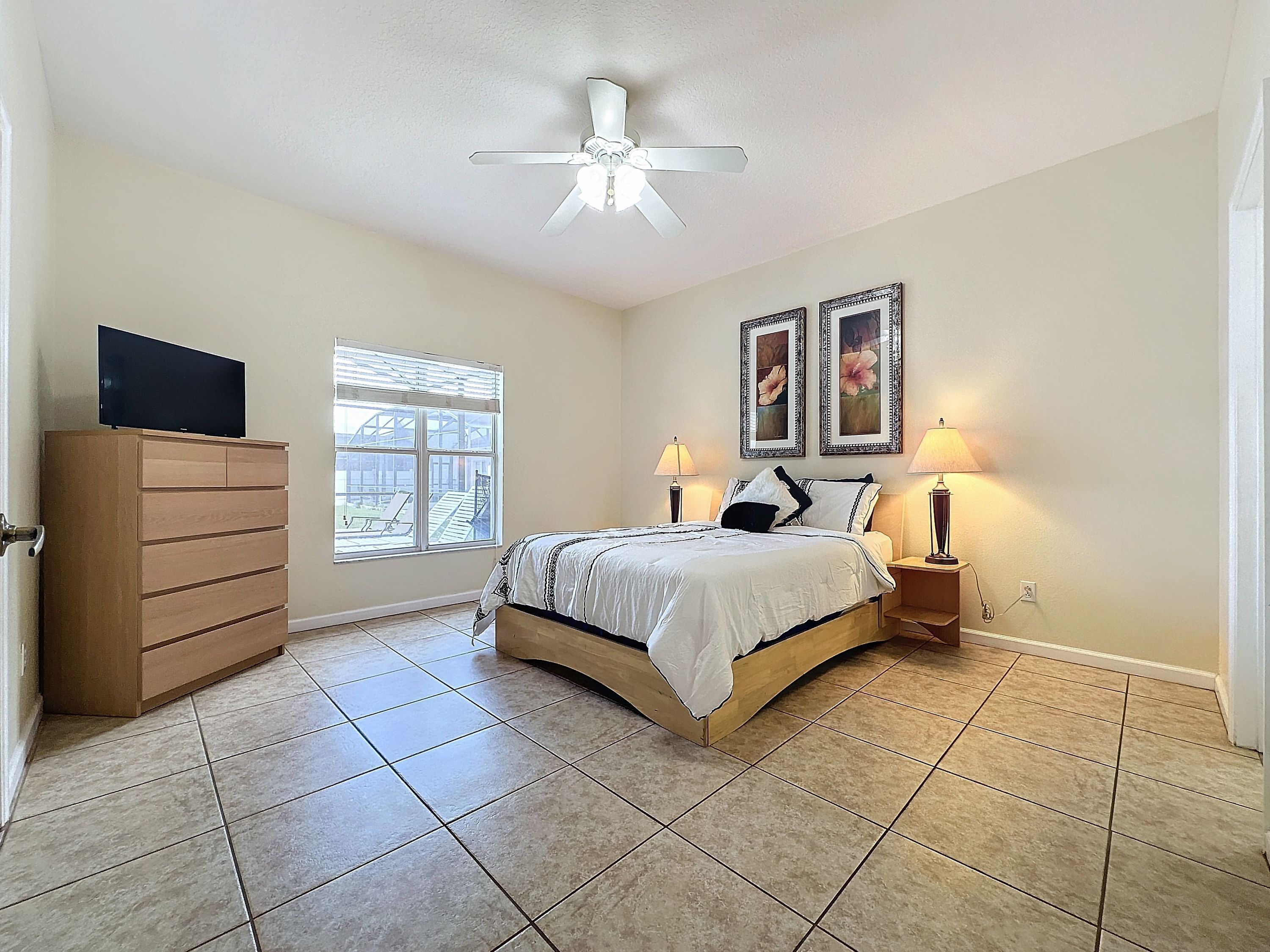 Quarto com cama, cômoda, ventilador de teto, janela e duas luminárias.