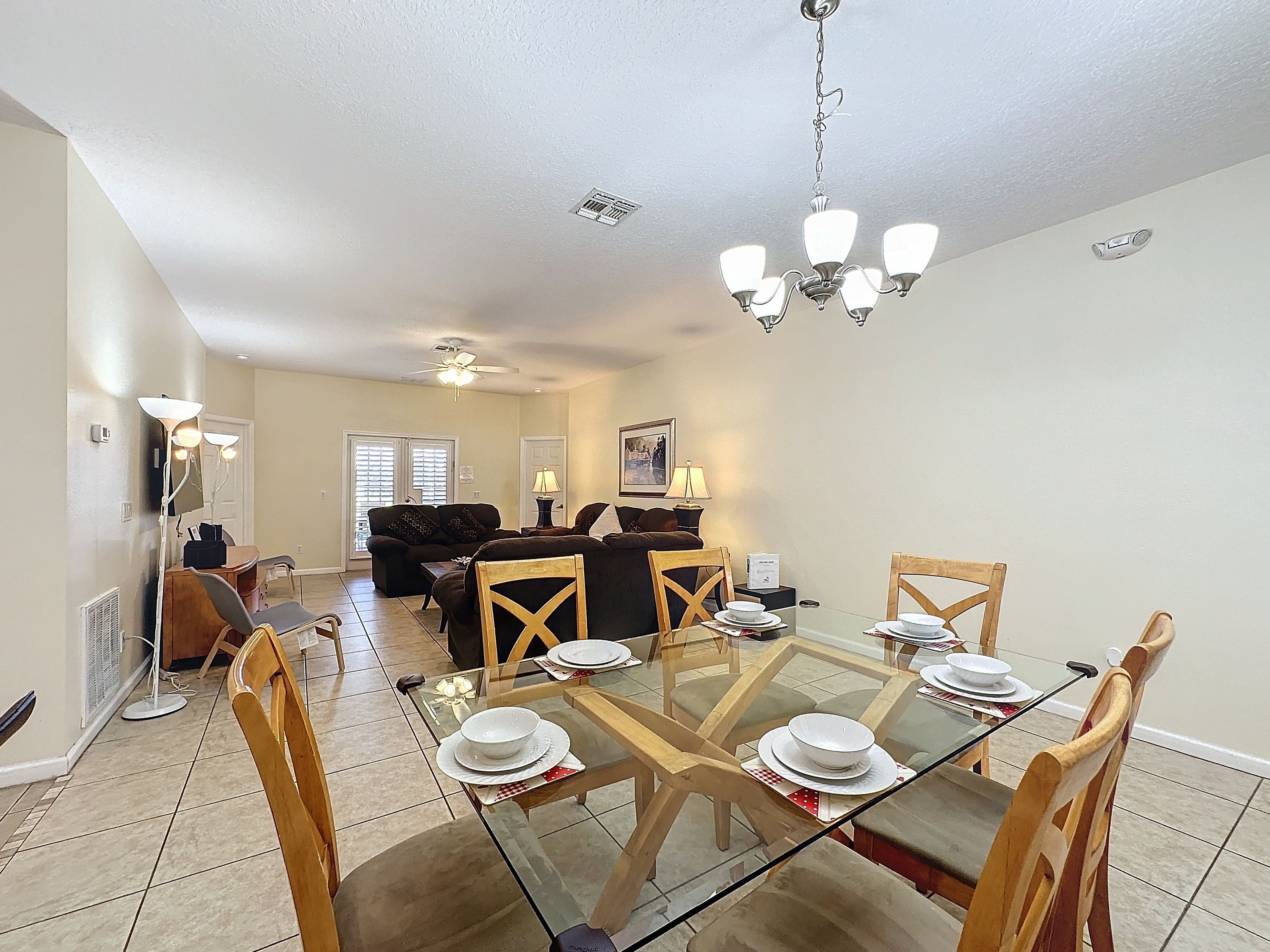 A dining area with a glass table, wooden chairs, and a sofa in the background.