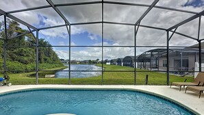 Piscina com cobertura de vidro, vista para um rio e área gramada com uma cadeira.