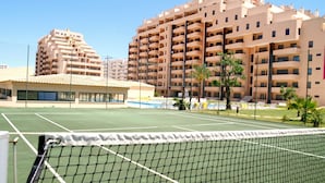 En tennisplan med ett nät i förgrunden, omgiven av höghus med balkonger.