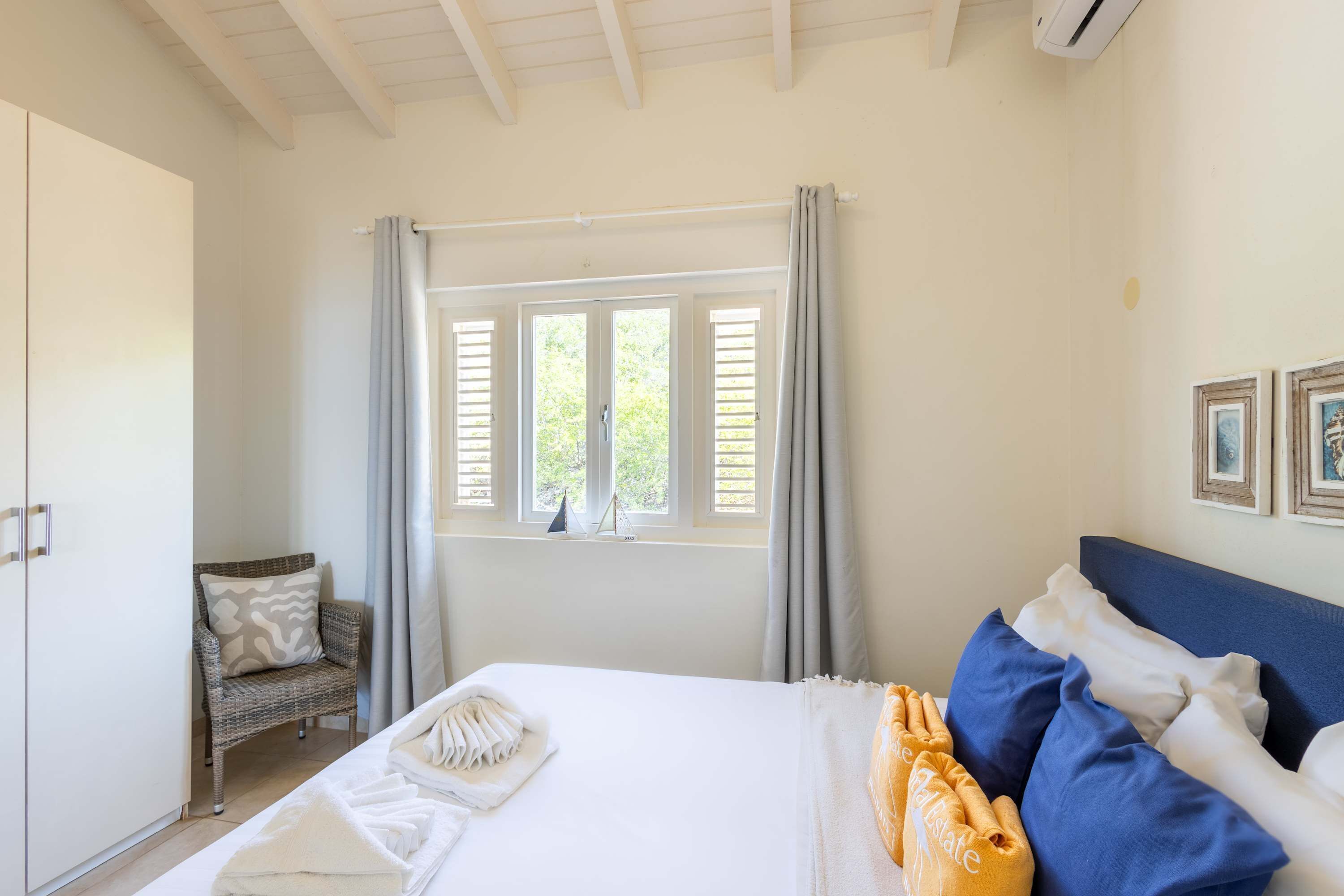 A bedroom with a bed, a chair, a window with curtains, and a wall with framed pictures.
