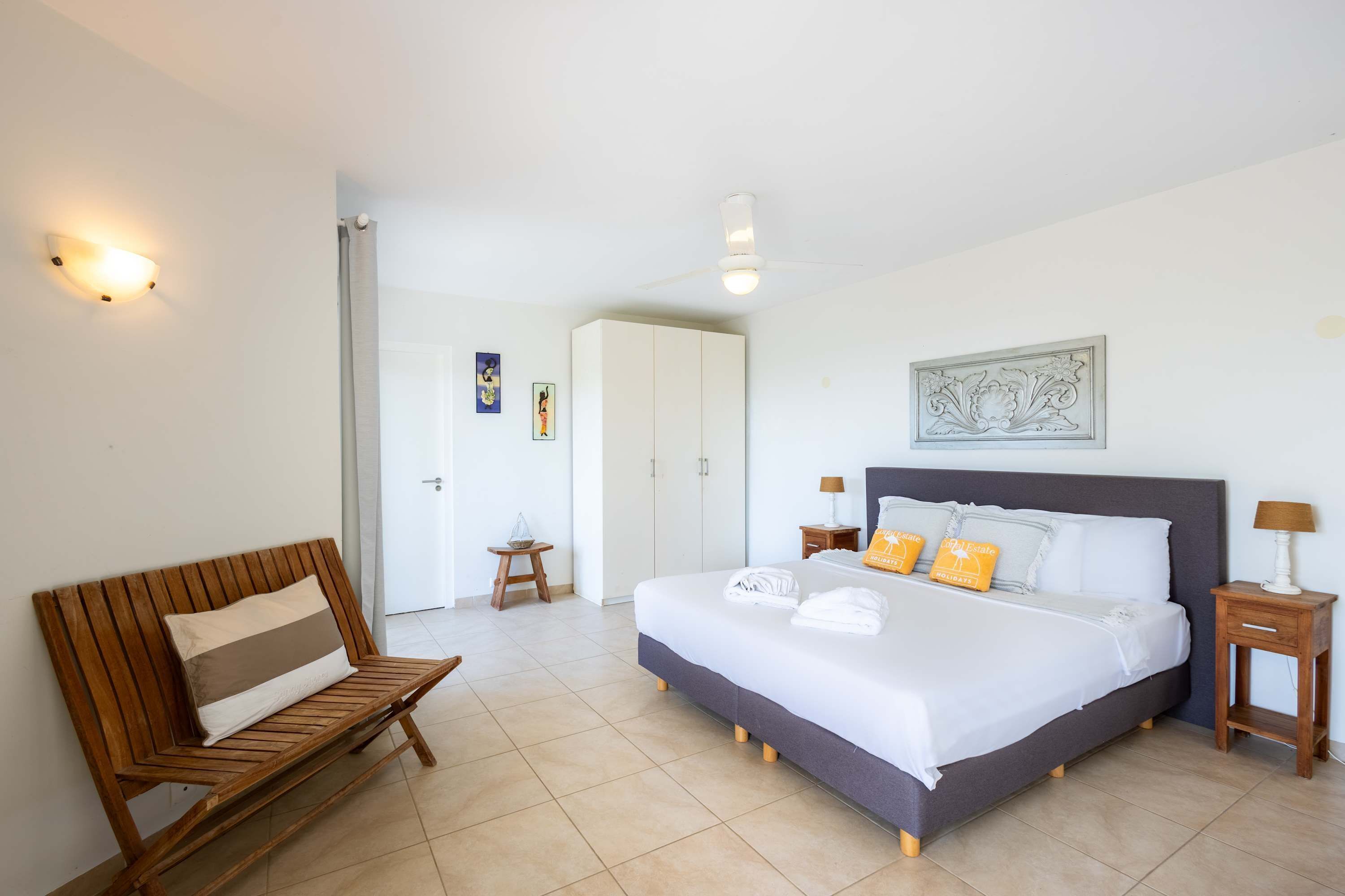 Habitación de hotel con una cama, un banco de madera, una mesita y una puerta que da a otra habitación.