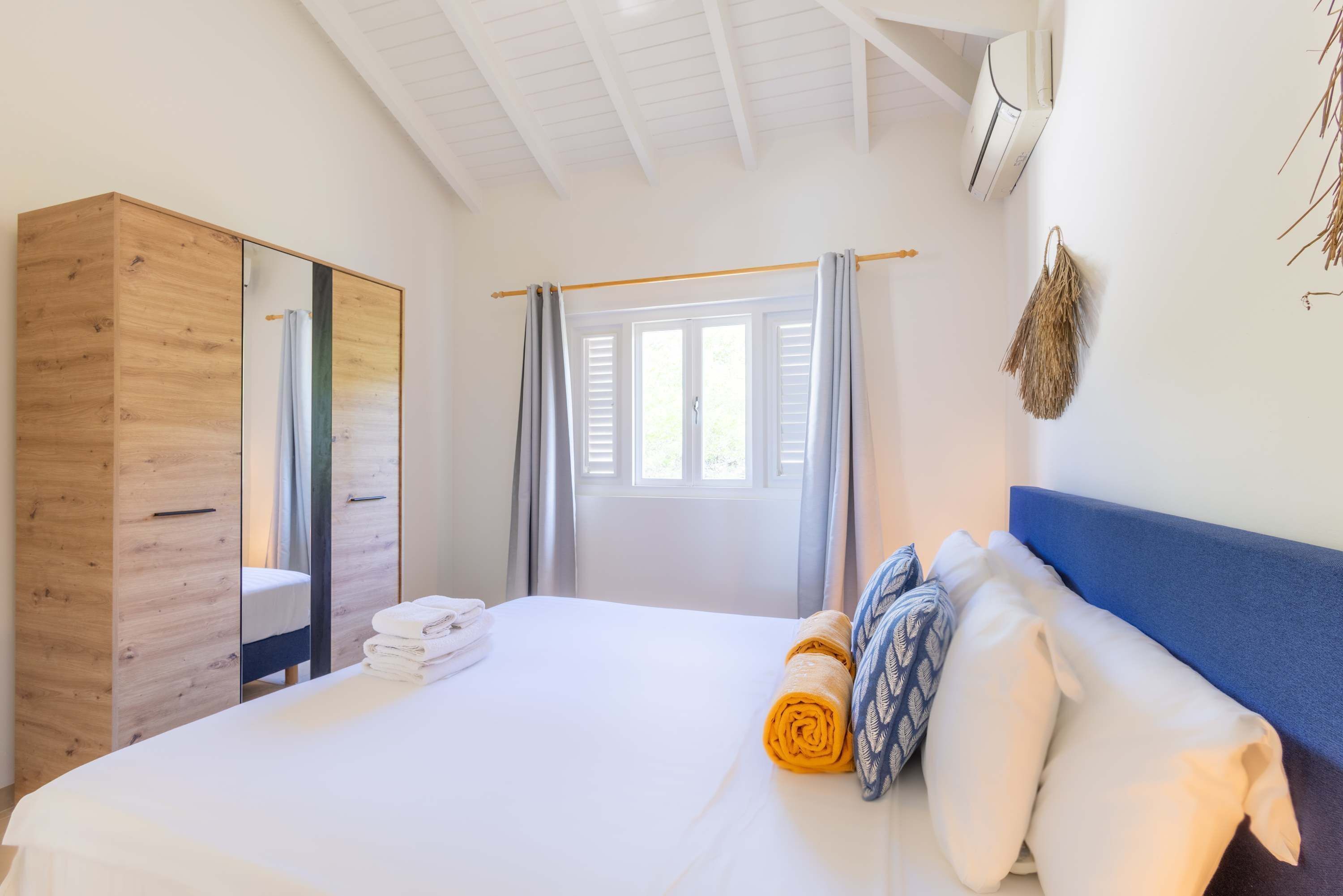 Ein Schlafzimmer mit Bett, Kleiderschrank, einem Fenster mit Vorhängen und einer Wand-Klimaanlage.