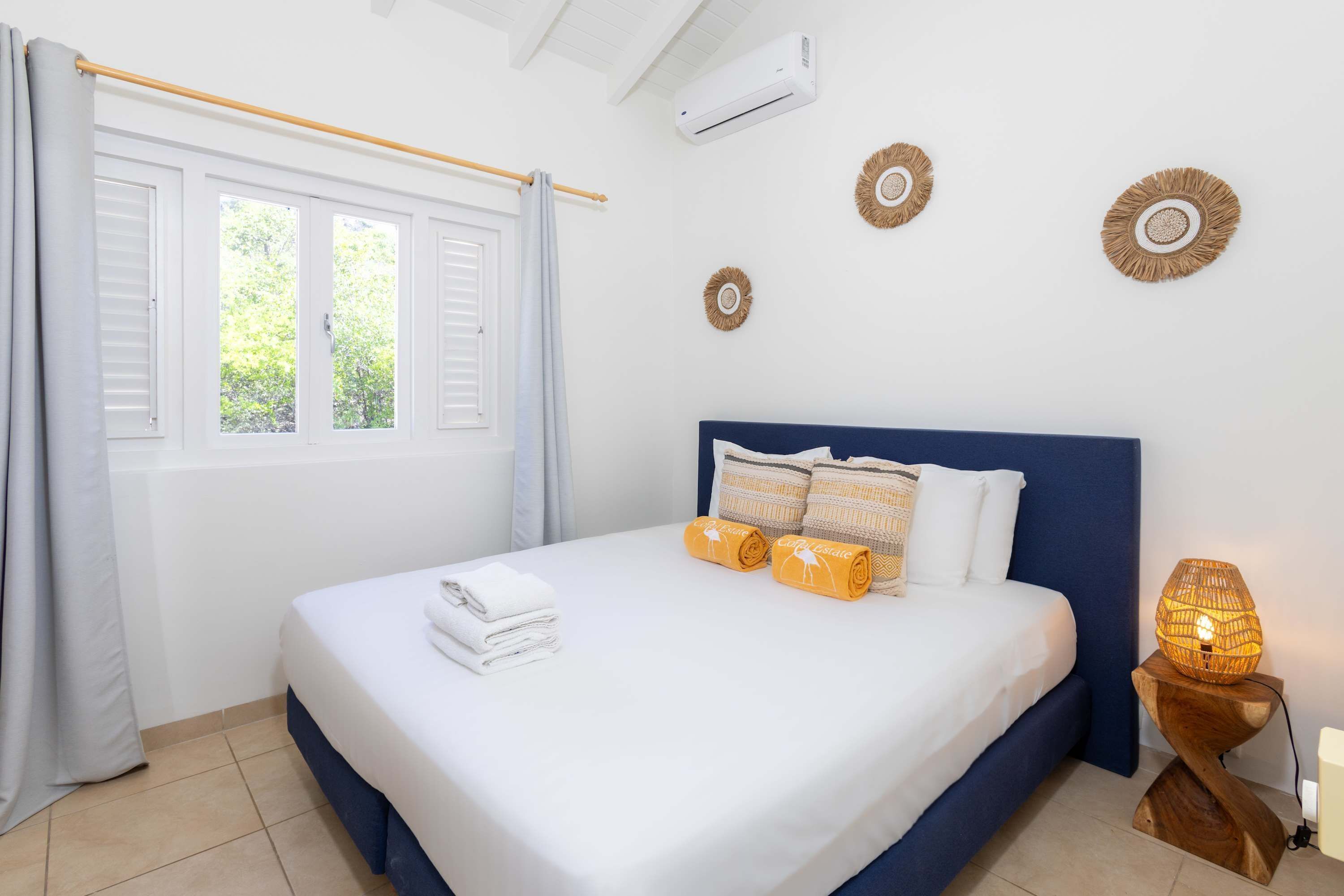 A neatly made bed with white linens and rolled towels, a bedside lamp, and wall decor.