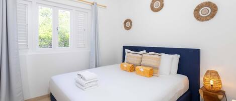 A neatly made bed with white linens and rolled towels, a bedside lamp, and wall decor.