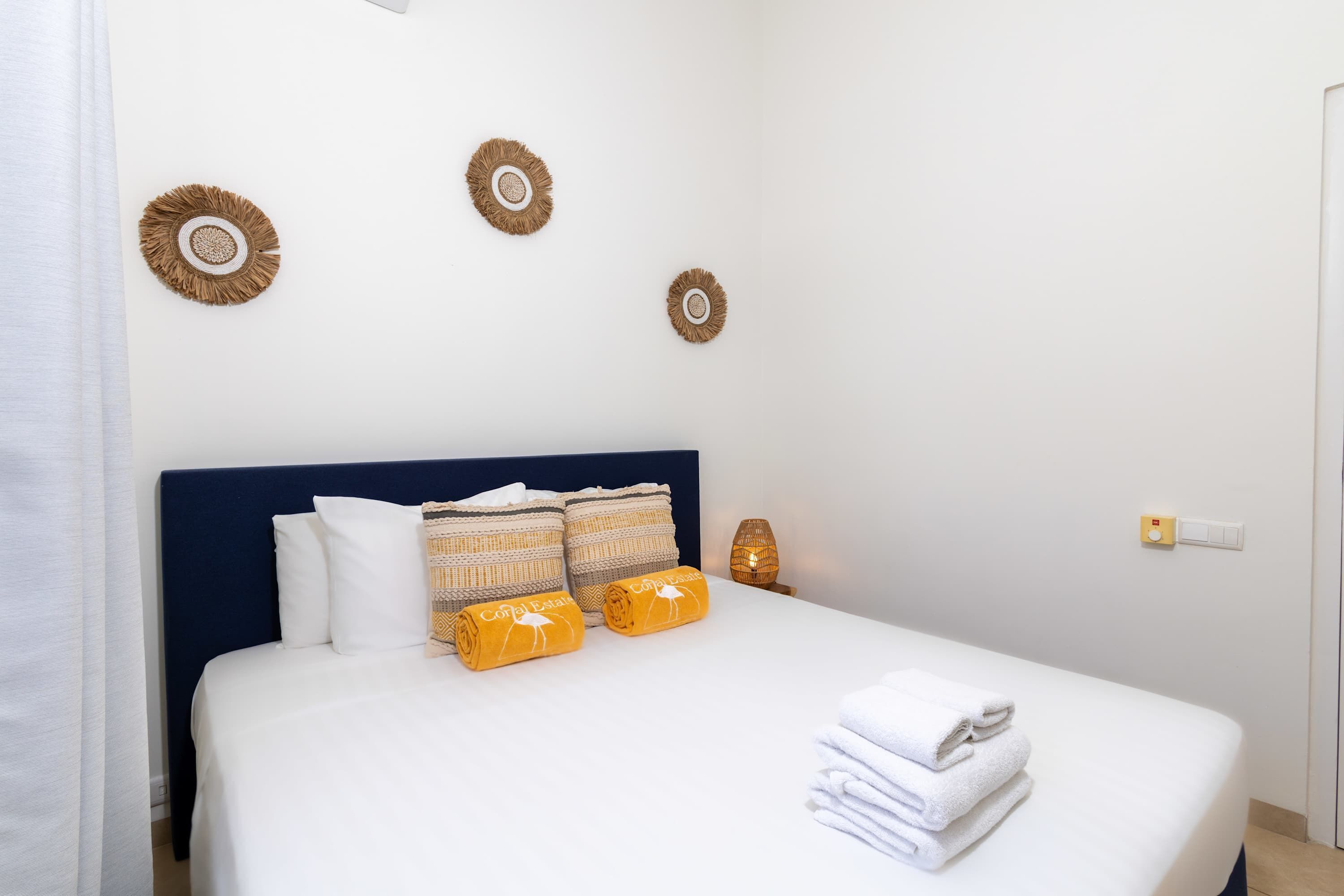 A neatly made bed with white linens, two yellow towels, and a stack of white towels.