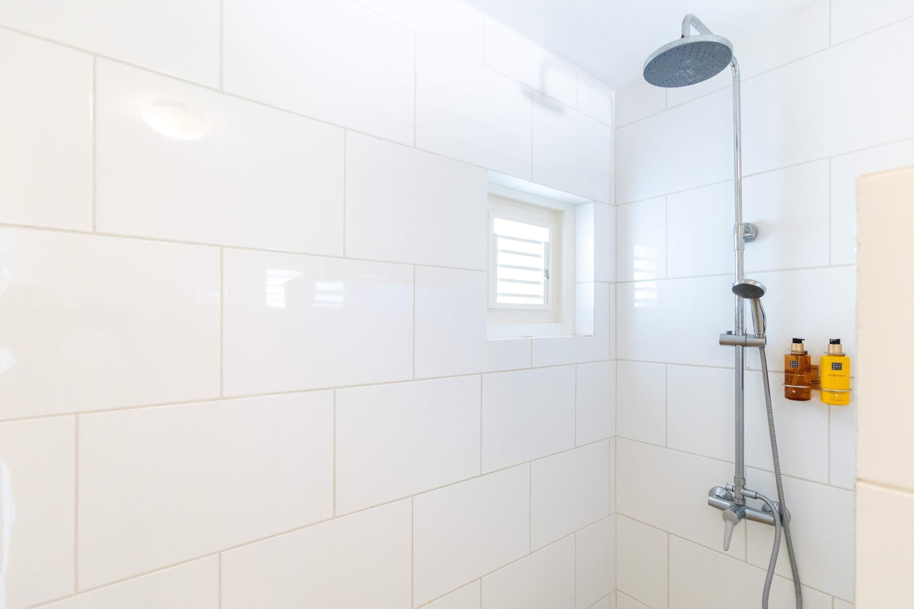 A bathroom with white tiles, a shower, and two bottles of shampoo on the wall.