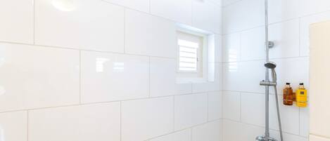 A bathroom with white tiles, a shower, and two bottles of shampoo on the wall.