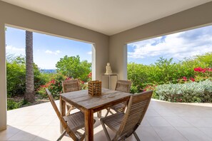 A patio with a wooden table and chairs, a white sculpture, and a view of greenery and the sea. - Endless Summer in Jan Kok (Sint Willibrordus)