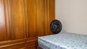 Un dormitorio con un armario de madera, una cama con colcha estampada y un ventilador de pie.