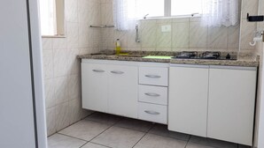 Una cocina con armarios blancos, encimera de granito y una ventana con cortinas de encaje.
