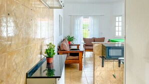A compact living space with a kitchenette, a dining area, and a window with curtains. - Tima Casa com Wifi pr Ximo a Praia em Itanha m SP (Itanhaém)
