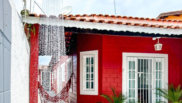 A red building with a white door and windows, a showerhead, and potted plants. - Tima Casa com Wifi pr Ximo a Praia em Itanha m SP (Itanhaém)