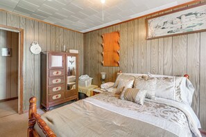 Camera da letto con parete rivestita in legno, un letto con biancheria a motivi, un comò in legno e un quadro incorniciato sopra il letto.