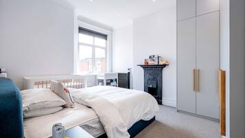 A modern bedroom with a large bed, a radiator, a bookshelf, and a wardrobe.