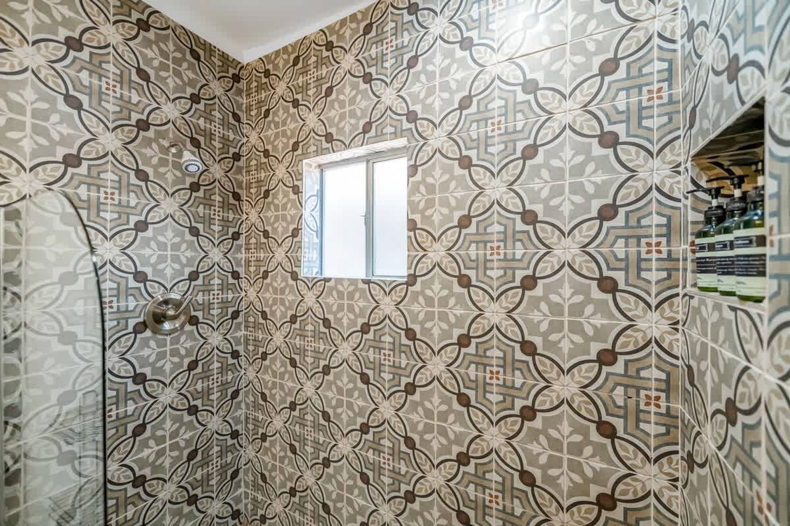 Un baño con pared de baldosas estampadas y una ventana.