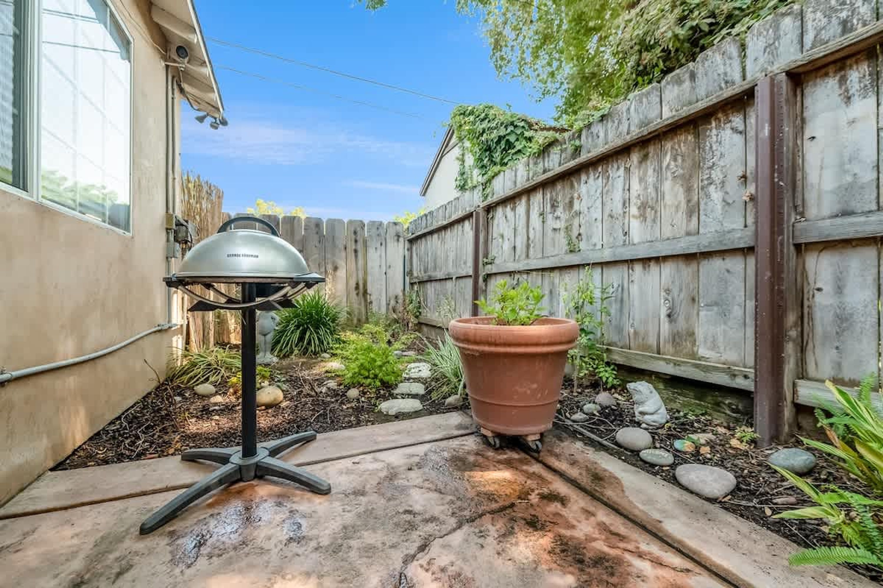 A patio area with a barbecue grill, a potted plant, and a wooden fence.