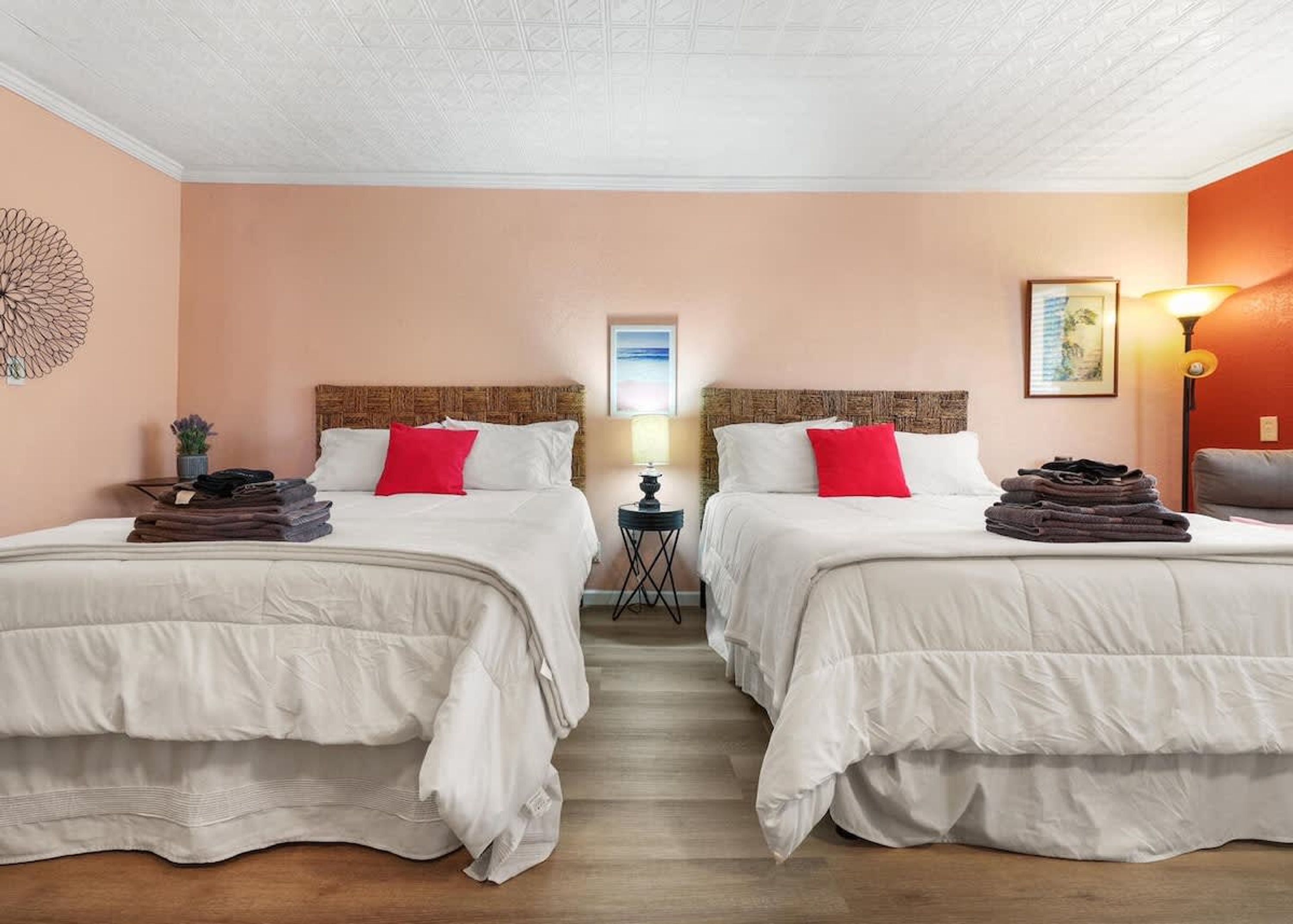 Een hotelkamer met twee bedden, een klein tafeltje met een lamp en een decoratief wandobject.