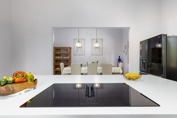 A modern kitchen with a central island, a dining area with a wooden cabinet, and a black refrigerator.