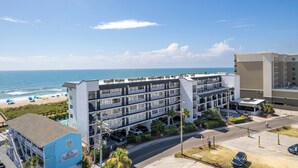 A multi-story hotel with a parking garage, located near a beach with umbrellas and a view of the ocean. - Carolina Beach Condo w/ Marina View, on Boardwalk (Carolina Beach)